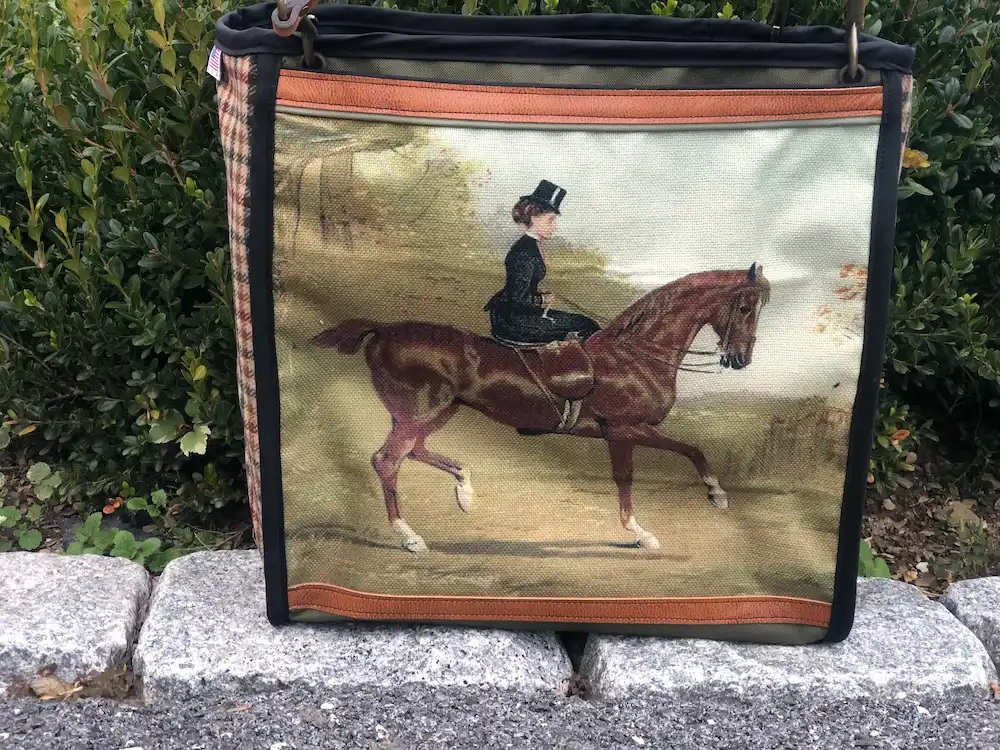 Custom black tote bag featuring a detailed illustration of a brown horse and rider, resting on a stone ledge with a leather shoulder strap.