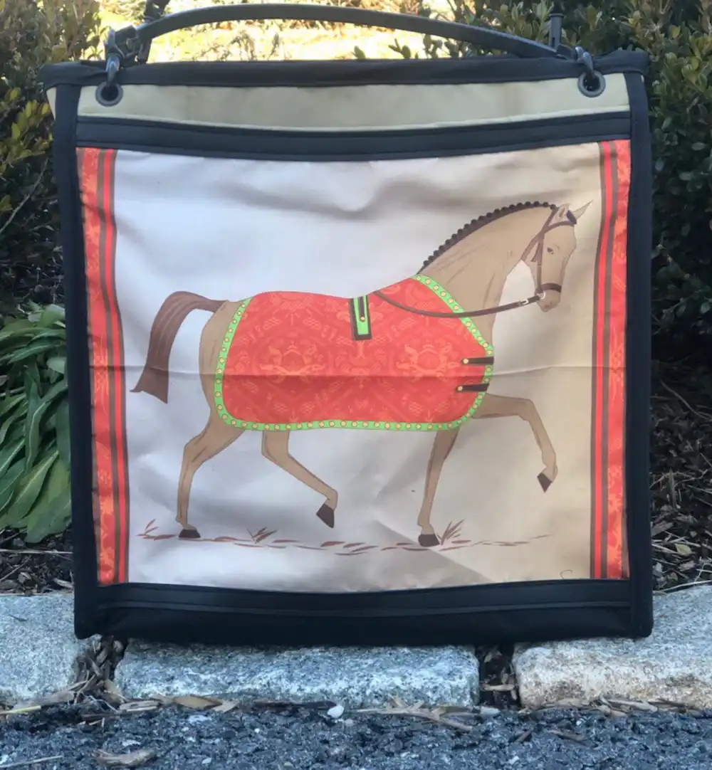 Custom black tote bag featuring a detailed illustration of a horse with a red coat, resting on a stone ledge with a leather shoulder strap.