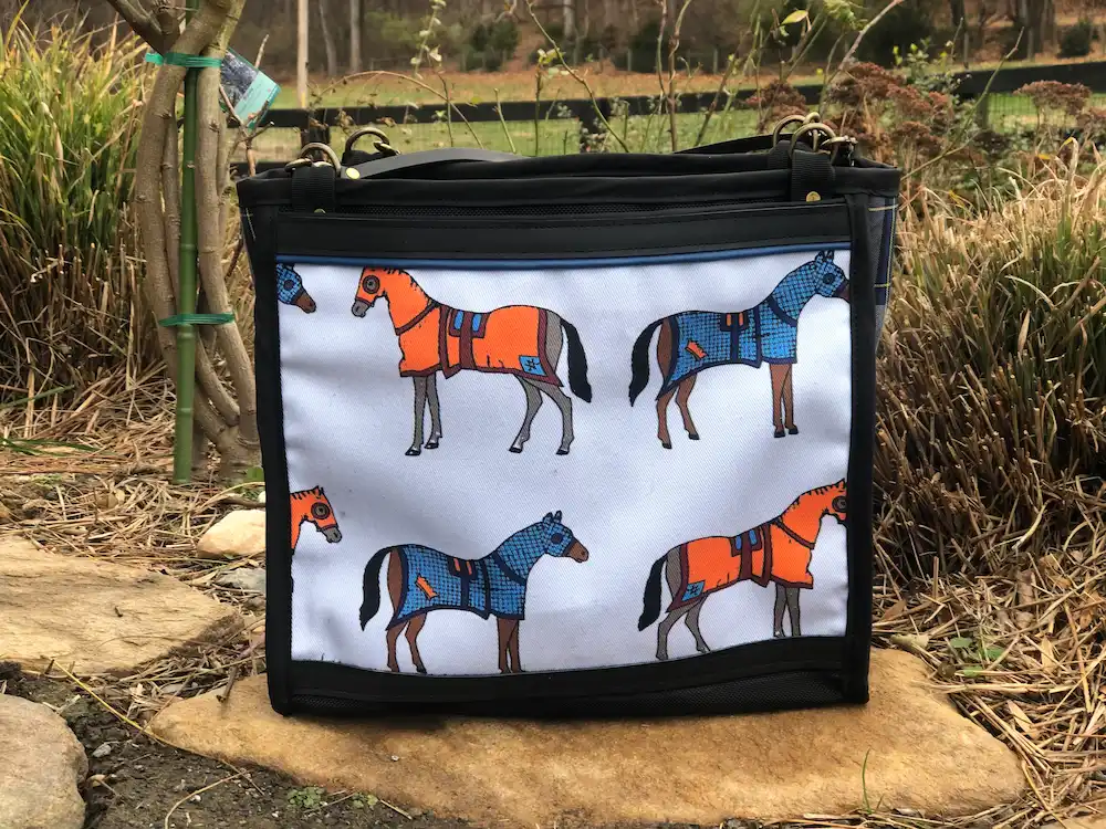 Custom black tote bag featuring a detailed illustration of horses wearing orange and blue coats, resting on a stone ledge with a leather shoulder strap.