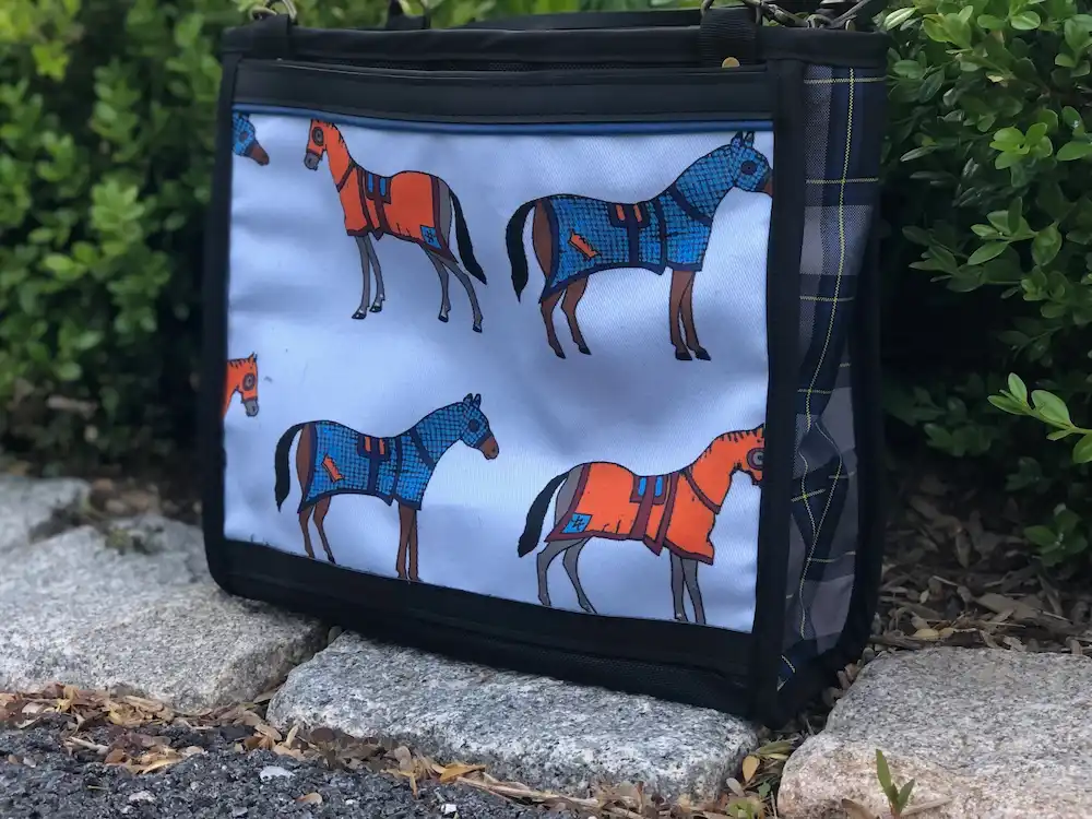 Custom black tote bag featuring a detailed illustration of horses wearing orange and blue coats, resting on a stone ledge with a leather shoulder strap.
